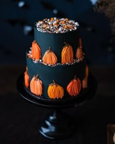 a three tiered cake decorated with pumpkins and sprinkles on a black plate