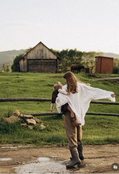 a woman holding a baby in her arms while standing on a dirt road near a fence