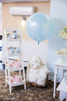 a white teddy bear sitting in a chair next to a blue balloon and other decorations