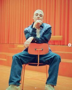 a man sitting on top of a red chair in front of an orange stage curtain