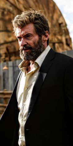 a man with a beard wearing a suit and white shirt is standing in front of a building