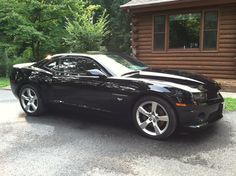 a black chevrolet camaro parked in front of a log cabin