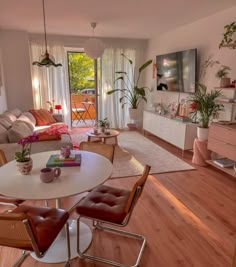 a living room filled with furniture and a white table surrounded by brown leather chairs on top of hard wood flooring