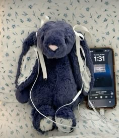 a blue stuffed animal sitting on top of a bed next to an mp3 player