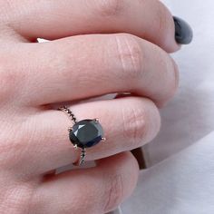 a woman's hand wearing a ring with a black diamond on the middle finger