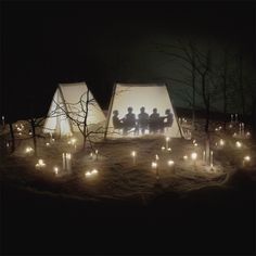 three people are standing in front of some tents with candles on the ground at night