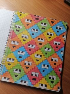 a notebook with colorful designs on it sitting on top of a wooden table next to a pen