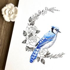 a blue bird sitting on top of a wooden table next to flowers and a white rose