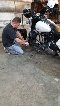 a man working on a motorcycle in a garage with his dog sitting next to it