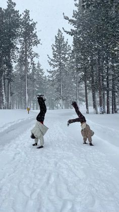 two people are playing in the snow near some trees