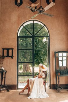 a woman sitting on a chair in front of an open door wearing a large hat