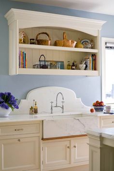 a kitchen with blue walls and white cabinetry, marble counter tops and open shelves