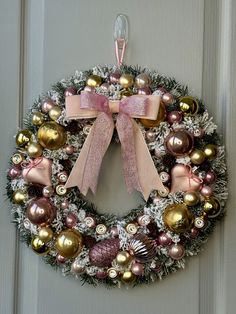 a christmas wreath hanging on the door with ornaments around it and pink ribbon tied to it