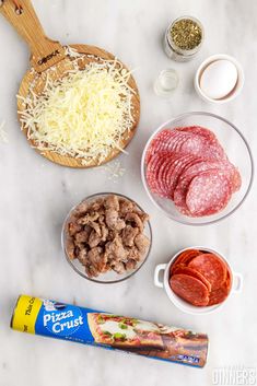 ingredients to make pizza including meat, cheese and pepperoni on a marble counter top