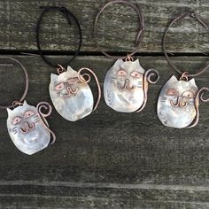 four metal cats hanging from brown cords on a wooden surface with one cat's face painted on it