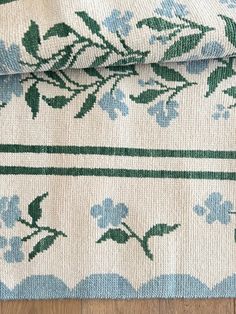 two pieces of fabric with blue flowers and green leaves on them sitting on top of a wooden floor