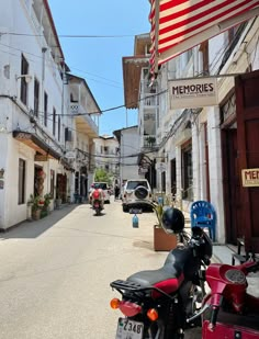 motorcycles parked on the side of an empty street with people walking by and american flag hanging from buildings