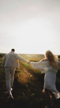 two people are running in the grass holding hands and looking at each other with their arms outstretched