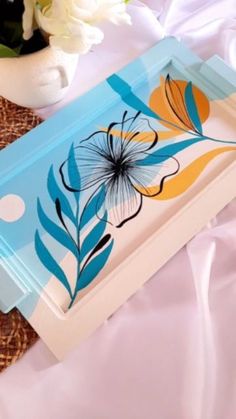 a blue tray with flowers on it sitting on a white table cloth next to a vase