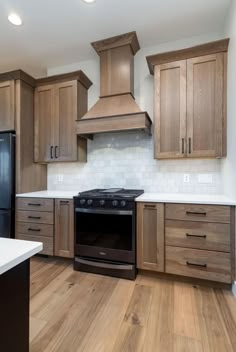 an empty kitchen with wooden cabinets and black stove top oven in the center, surrounded by white marble counter tops