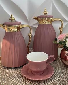 two pink vases sitting next to each other on top of a table with a cup and saucer