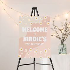 a welcome sign sitting on top of a easel next to a vase with flowers