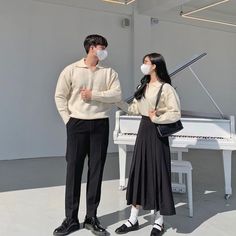 a man and woman standing in front of a white piano wearing masks to protect them from the corona