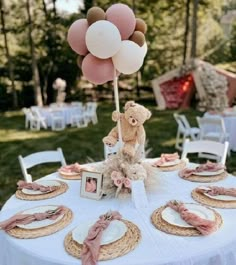 a teddy bear sitting on top of a table with plates and balloons in the air