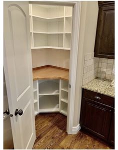 an empty pantry in the corner of a kitchen with wood floors and cabinets on either side