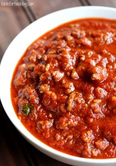 a white bowl filled with chili sauce on top of a wooden table next to a spoon