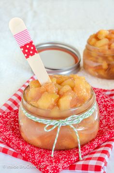 a jar filled with apples sitting on top of a red and white checkered cloth