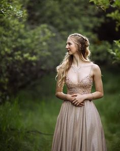 a woman in a long dress standing in the woods looking back at something she is wearing