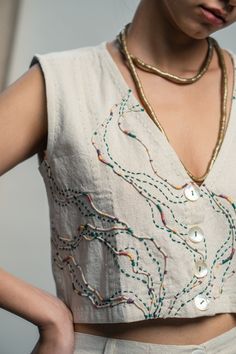 a woman wearing a white top with beads on it