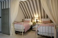 two beds in a room with striped walls and white drapes on the top of them