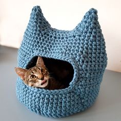 a cat laying in a blue crocheted bed on top of a white table