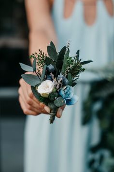 a woman holding a bouquet of flowers in her hand and wearing a blue dress behind her