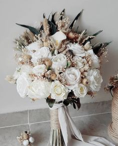 a bridal bouquet with white flowers and greenery on the floor next to a rope