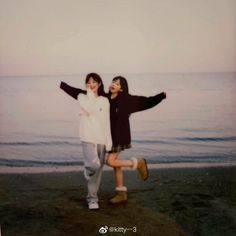 two people are standing on the beach with their arms spread out in front of them