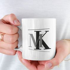 a woman holding a white coffee mug with the letter k on it in her hands