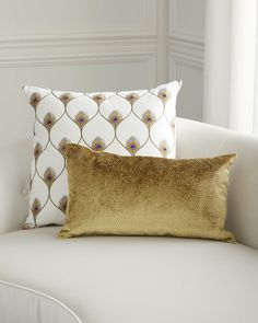 two pillows sitting on top of a white couch in front of a window with gold sequins