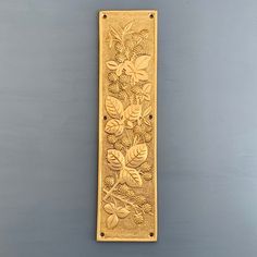 an ornate brass door handle with leaves and berries on the front, against a gray background