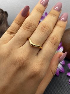 a woman's hand with a gold ring on her finger and purple flowers in the background