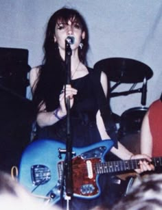 a woman singing into a microphone while holding a blue guitar in front of her face