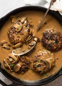 some meat patties and mushrooms are in a skillet with gravy on the side