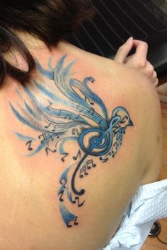 the back of a woman's shoulder with music notes on it and a bird tattoo