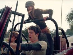 two people sitting in the back of a truck and one person standing on top of it