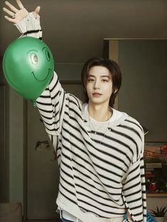 a young man holding a green ball in his hand while wearing a striped shirt and jeans