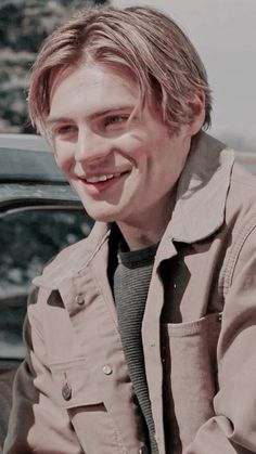 a young man sitting in front of a car smiling