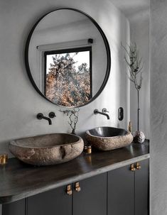 two sinks in front of a round mirror on the wall above them are black faucets