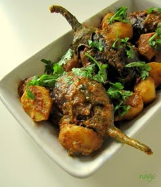 a white plate topped with meat covered in green garnish and potatoes on top of a table